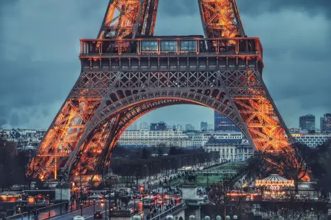 Eiffel rozświetlona pomarańczowym blaskiem, z widokiem na paryskie ulice i budynki.