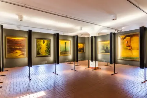 Wystawa obrazów Beksińskiego w galerii, z widocznymi dziełami w żółtych i brązowych barwach.