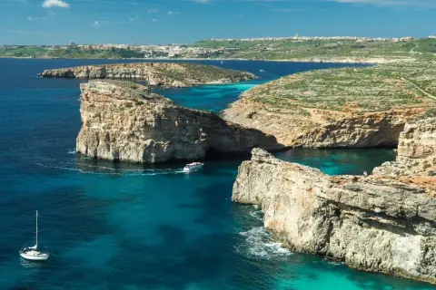 Malta zima: turkusowe wody, skaliste klify i łodzie kołyszące się na falach. W oddali widać miasto.