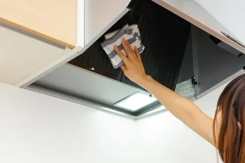 Mano limpiando campana extractora por fuera con un paño a rayas.