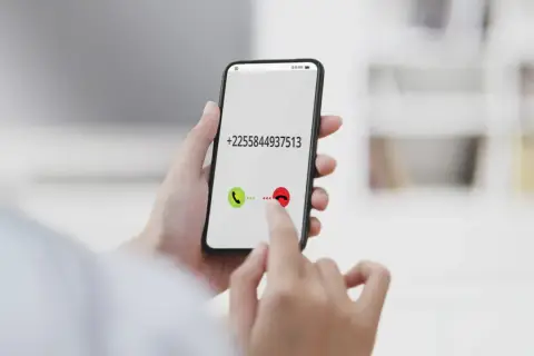 Dłoń trzyma smartfon z numerem +2255844937513. Palec wskazuje przycisk odbierania połączenia, jakby wybierał kierunkowy 40.