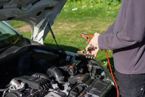 Ręce trzymające kable rozruchowe przy akumulatorze. Czy można odpalic auto na wlaczonym prostowniku?