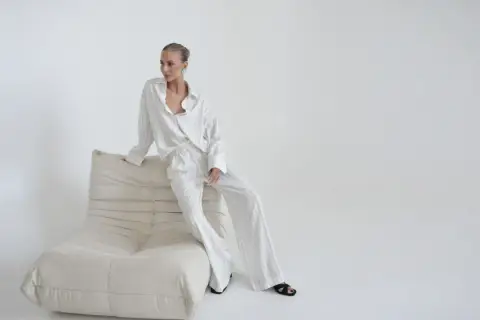 Elegancka kobieta w pasiastym komplecie, uosobienie quiet luxury, siedzi na kremowej sofie.