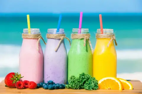 Cztery kolorowe smoothie na plaży: różowe, fioletowe, zielone i żółte. Idealne na lato, pokazują, jak zrobić smoothie z owoców i warzyw.