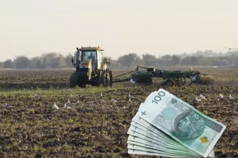 Młody rolnik pracuje na polu, za nim widać pług i stos banknotów 100 zł. Ptaki krążą nad ziemią.