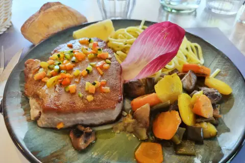 Pavé de thon poêlé, garni de dés de légumes croquants, servi avec des pâtes, des légumes racines et une feuille de chicorée. Une recette savoureuse.