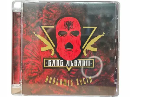Okładka płyty CD "Królowie życia" zespołu Gang Albanii. Czerwona kominiarka z orłem, złote kałasznikowy i mroczne tło.