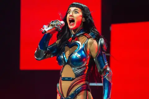 Katy Perry w błyszczącym, niebiesko-srebrnym kostiumie z sercem na piersi śpiewa na scenie w Krakowie.