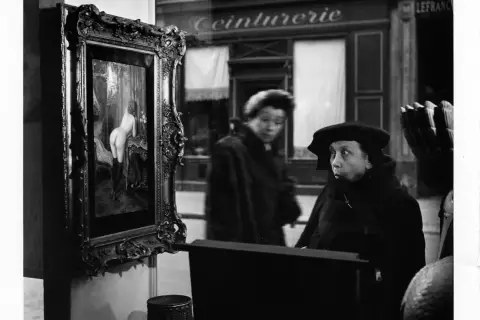 Una donna guarda un quadro in una vetrina, un'altra figura sfocata sullo sfondo. Robert Doisneau foto.