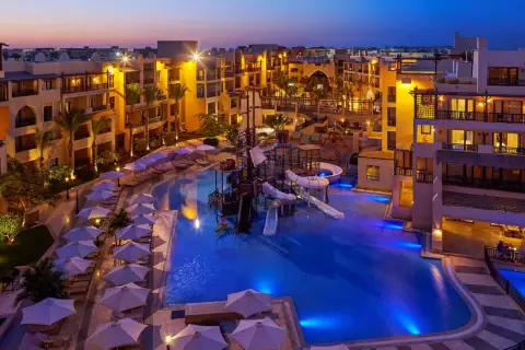 Wieczorem w Steigenberger Aqua Magic, basen z atrakcjami wodnymi i zjeżdżalniami, otoczony hotelowymi budynkami i leżakami pod parasolami.