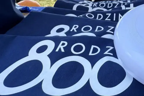 Granatowe koszulki z napisem "RODZINA 800 plus" i biały frisbee z logo 800 plus.