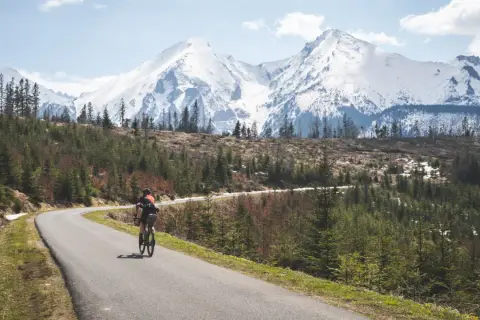 Rowerzysta na krętej drodze z widokiem na ośnieżone Tatry. Marzenie o rowerem dookoła Tatr w jeden dzień staje się rzeczywistością.