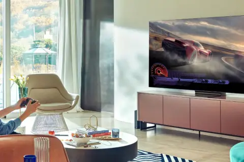 Młody mężczyzna gra w grę wyścigową na telewizorze 65 cali. Idealna odległość od telewizora 65 cali zapewnia wciągające wrażenia.