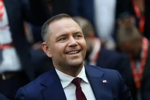 Uśmiechnięty mężczyzna w garniturze z polską flagą na klapie. Czy to jego styl życia wyjaśnia, dlaczego urząd prezydenta jest uznawany za najdroższy w utrzymaniu w całej Europie Środkowej?