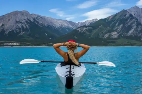 Frau im Kajak auf türkisfarbenem See, Berge im Hintergrund. Ein Symbol für das Erreichen von finanzieller Freiheit und ein Leben voller Abenteuer.