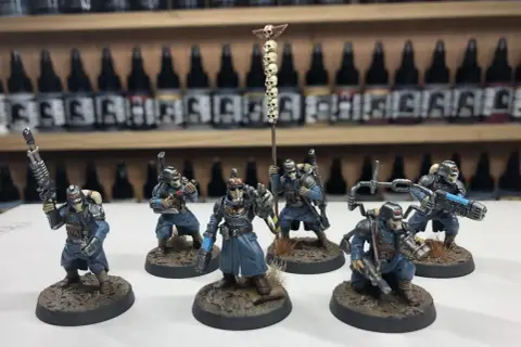 Krieg command squad w niebieskich mundurach, z karabinami i sztandar z czaszkami, gotowi do walki.