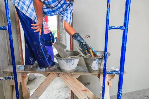 Pracownik na rusztowaniu przygotowuje zaprawę. Tynkowanie ścian cena zależy od wielu czynników.