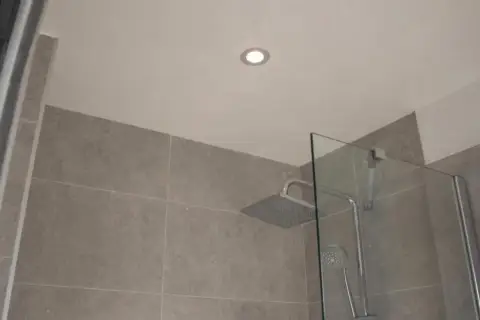 Nowoczesne oświetlenie nad prysznicem w łazience z szarymi płytkami i szklanym panelem.