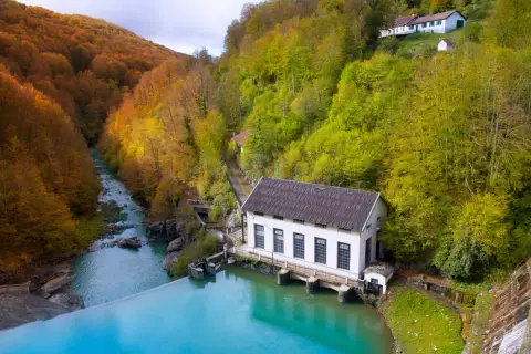 Embalse de agua turquesa junto a una central eléctrica, rodeado de bosques otoñales. Ideal para rutas selva de Irati.