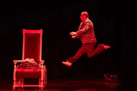 Aktor w skoku na scenie Teatru Komedia Kraków. Czerwone światło podkreśla dynamikę sceny.
