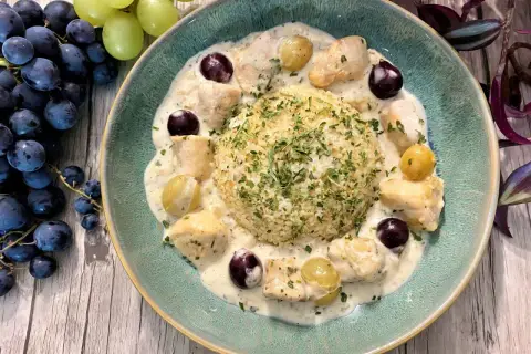 Un délicieux poulet au raisin crémeux, servi avec du riz et garni de persil frais. Des grappes de raisins noirs et verts complètent cette assiette appétissante.