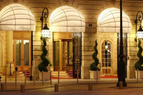 Eleganckie wejście do słynnego paryskiego hotelu Ritz, oświetlone latarniami i ozdobione spiralnymi drzewkami.
