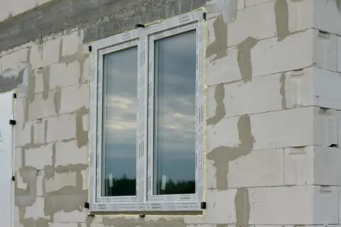 Okna w ścianie z bloczków betonowych, z widocznym pianką montażową. To maksymalny otwór bez nadproża, gotowy na dalsze prace budowlane.