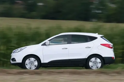 Biały Hyundai ix35 2.0 benzyna w ruchu, z rozmytym tłem zielonych pól i drzew.