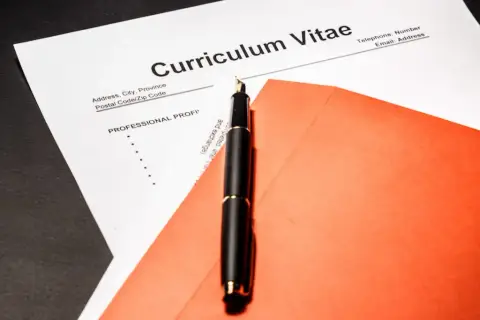 Eleganckie pióro na tle dokumentu Curriculum Vitae po angielsku i pomarańczowej koperty.