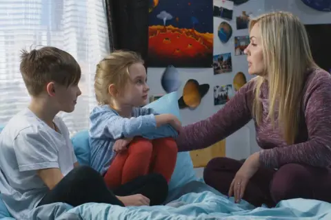 Kobieta z dwójką dzieci, otoczona plakatami kosmicznymi, rozmawia o przyczyny popularności motywu "found family" w literaturze przygodowej.