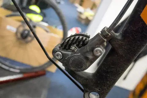 Close-up of a bicycle's hydraulic disc brake caliper, showing the brake fluid top and cooling fins.