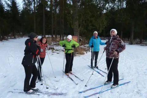 Grupa osób w strojach na narty biegowe przygotowuje się do jazdy w lesie.