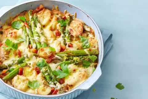 Herzhafter Spargel Auflauf mit Kartoffeln, Speck und geschmolzenem Käse, garniert mit Petersilie und Zitronenschale.