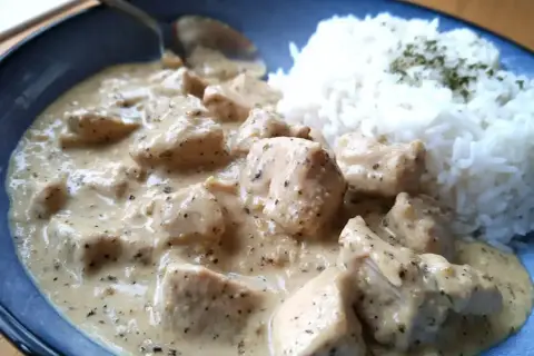 En krämig sås till kyckling och ris, med bitar av kyckling i en ljus sås. Riset är toppat med lite grön krydda.