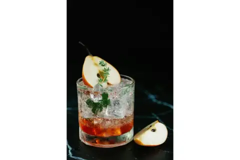 Un cocktail rafraîchissant avec une tranche de poire et une touche de thym, parfait pour un twist bière estival.