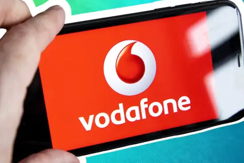 Vorsicht vor der neuen Betrugsmasche Vodafone! Ein Finger hält ein Smartphone mit dem Vodafone-Logo.