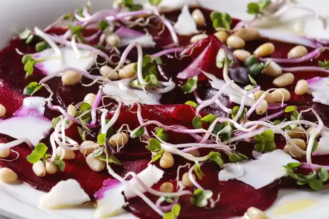 Carpaccio z buraka z kiełkami, orzeszkami pinii i białym serem. Kolorowe, świeże i apetyczne danie.