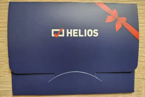 Chcesz wiedzieć, ile kosztuje voucher do kina Helios? Na zdjęciu widać elegancką, granatową kopertę z logo Helios i czerwoną wstążką, idealną na prezent.