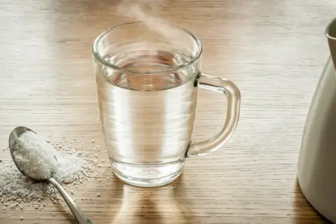 Łyżka soli i szklanka ciepłej wody, gotowe do płukania gardła solą.