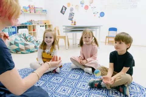 Dzieci biorą udział w zabawach integracyjnych w przedszkolu, siedząc na dywanie i słuchając nauczycielki.