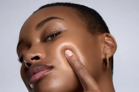 Piel oscura con un brillo dewy, resaltando sus pómulos y labios.