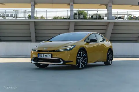 Nowy żółty Toyota Prius z nowoczesnym designem stoi na betonowym placu przed trybunami stadionu.