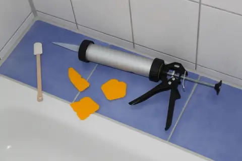 Pistolet do silikonu, szpachelki i drewniana łopatka gotowe do wymiany silikonu w kabinie prysznicowej.