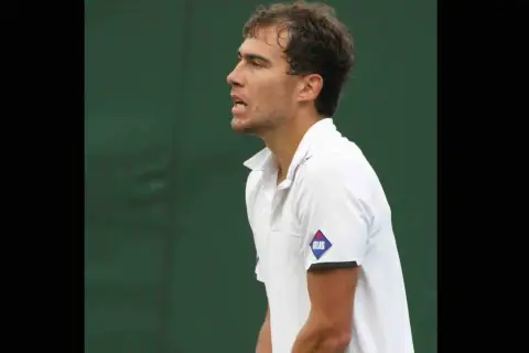 Jerzy Janowicz, z rakietą w dłoni, unosi palec wskazujący, świętując zwycięstwo. Jego majątek rośnie z każdym wygranym meczem.