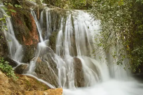 Cascadas de Hueznar, un velo de agua blanca desciende por rocas cubiertas de musgo y vegetación exuberante.