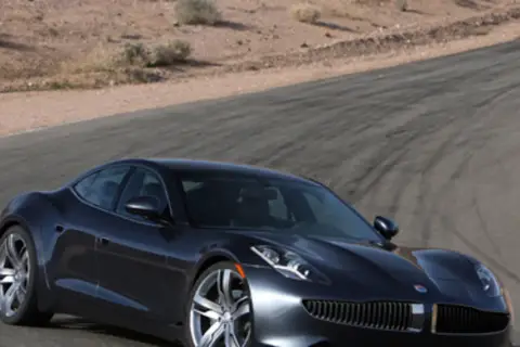 Elegancki, ciemnoszary Fisker Karma na torze wyścigowym, z pustynnym krajobrazem w tle.