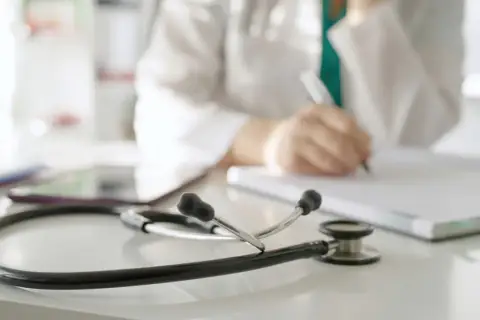 Lekarz rodzinny wypisuje receptę L4 na depresję. Na biurku leży stetoskop.
