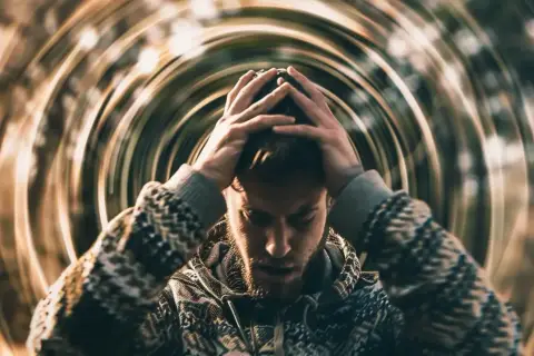 Mężczyzna z rękami na głowie, otoczony wirującymi liniami, symbolizującymi psychosomatykę i wewnętrzny niepokój.