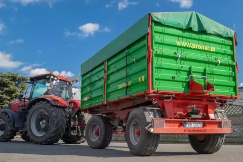 Czerwony traktor z zieloną przyczepą rolniczą. Zastanawiasz się, jak zarejestrować przyczepę rolniczą bez dokumentów? Sprawdź na www.pronar.pl.