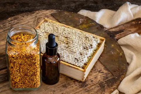 Słoik z pyłkiem pszczelim, buteleczka z kroplomierzem i plaster miodu. Naturalne składniki, które mogą posłużyć jako propolis lek.